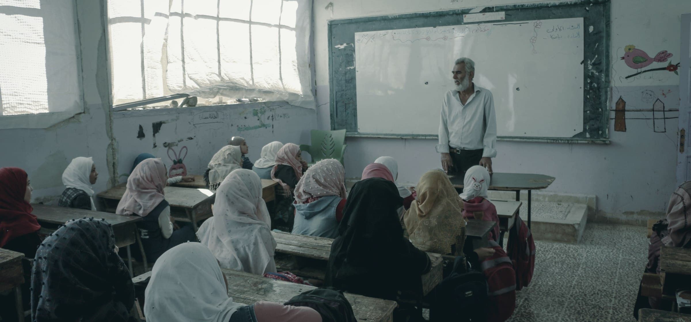 A teacher at a whiteboard addressing a classroom of girls in headscarves, Idlib, Syria