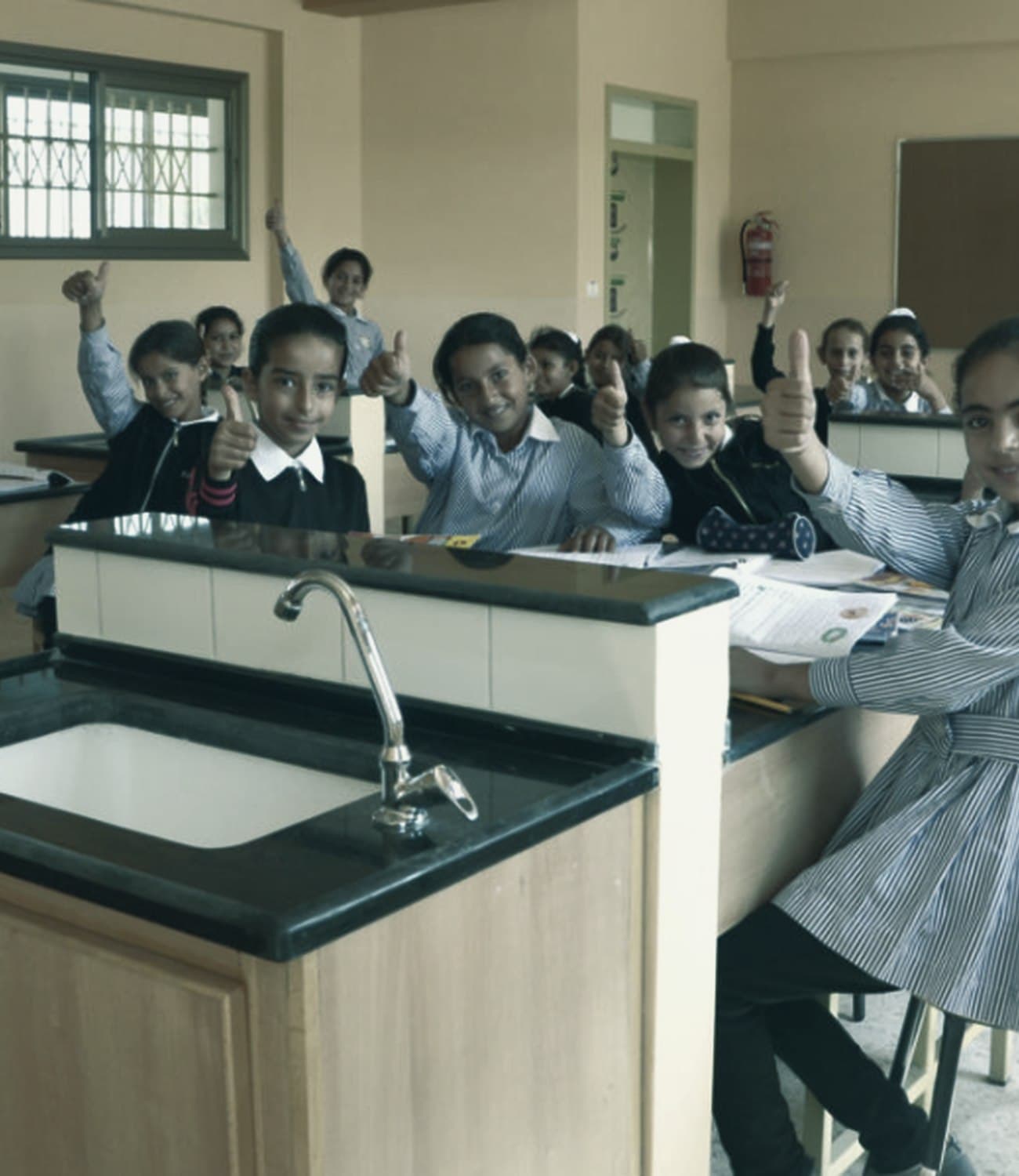 Schoolgirls in uniform raising their hands in a classroom